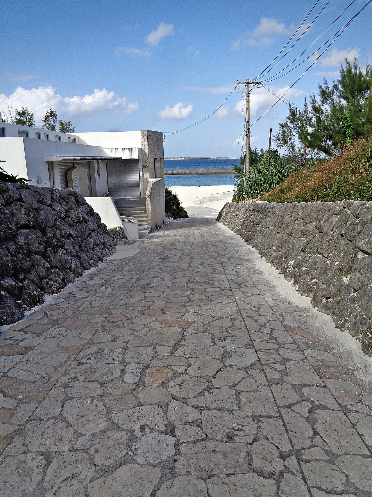 石畳の道の先に砂浜と海が見える水納島の風景(写真:ブルーノ・プラス / CC BY-SA 4.0)